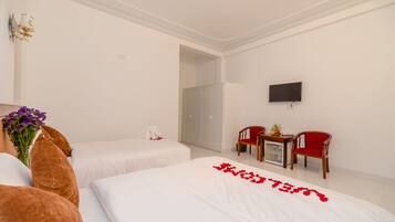 A hotel room with two beds, a TV, a desk with chairs, and a wardrobe.