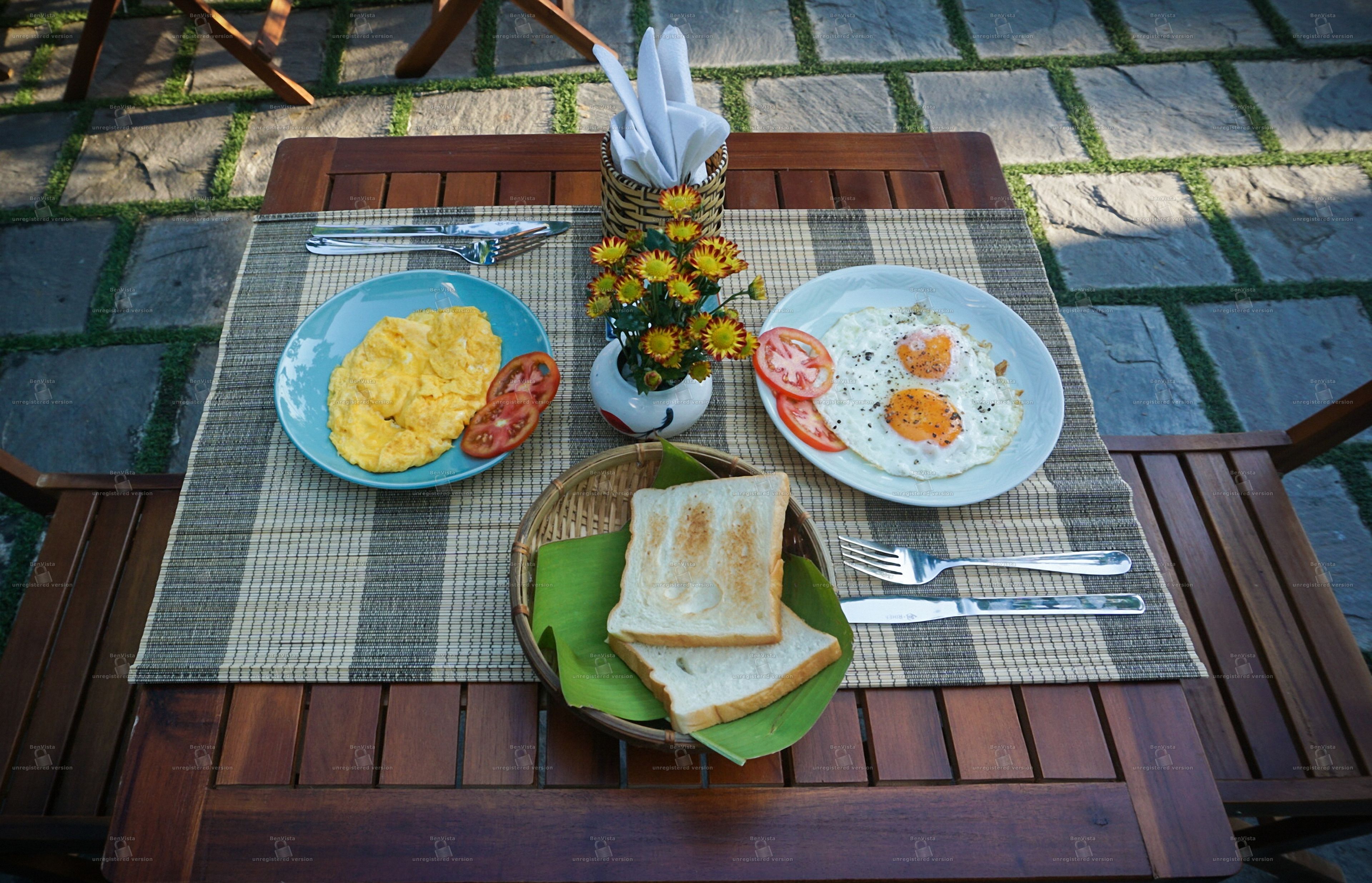 Un tavolo di legno con un sottopiattino, due piatti di cibo, un cesto di pane e un piccolo vaso con fiori.