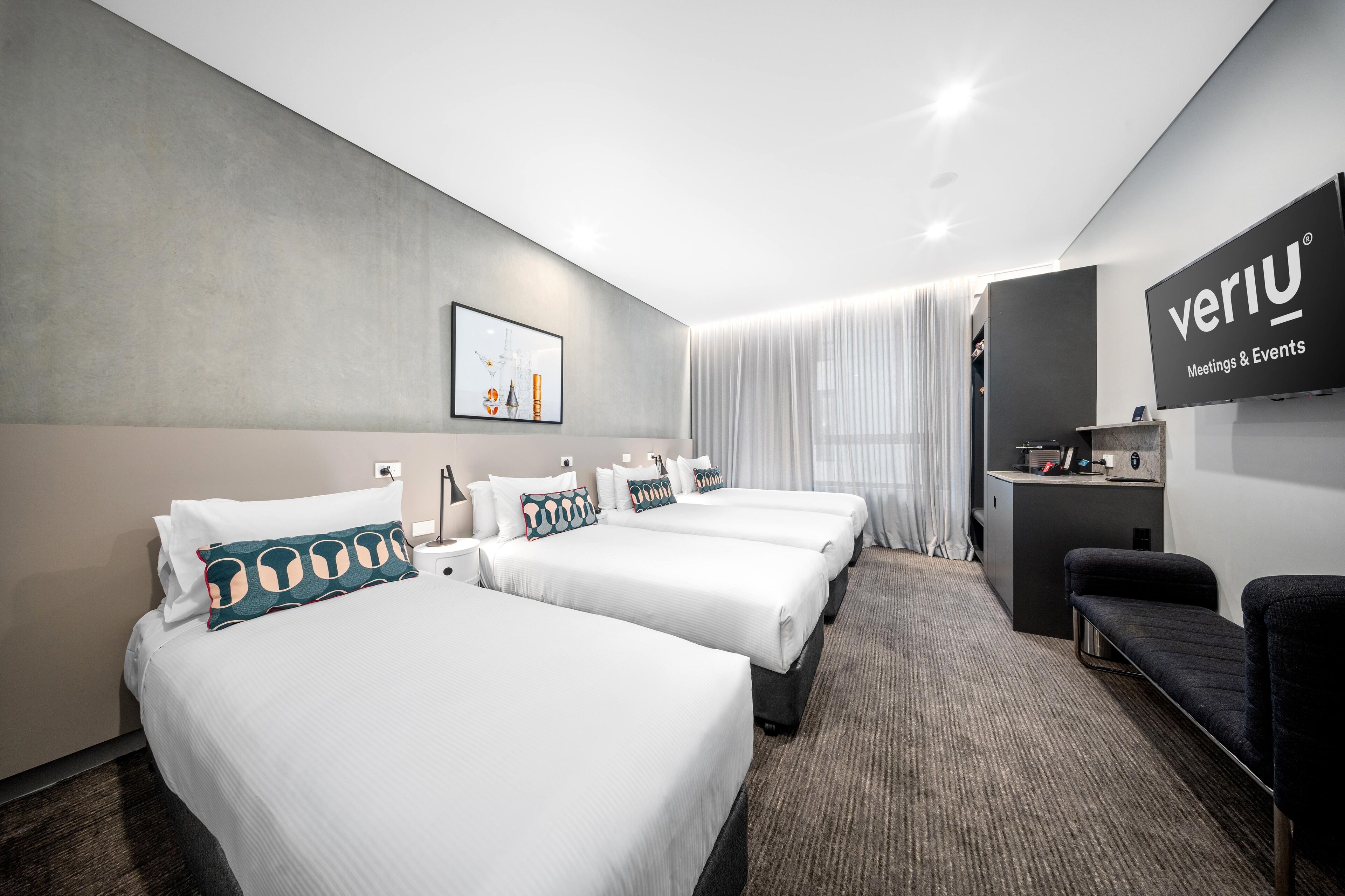 A hotel room with three beds, a desk, and a TV.