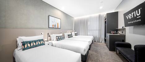 A hotel room with three beds, a desk, and a TV.
