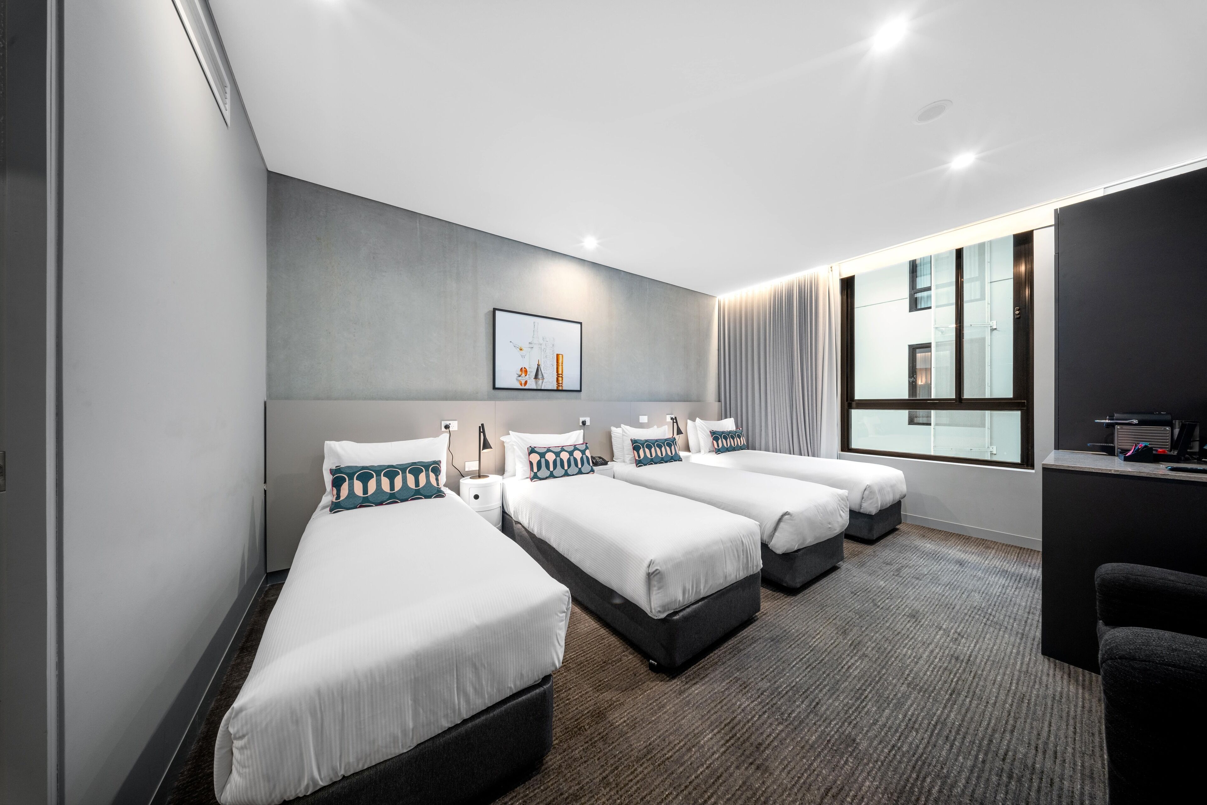 A hotel room with three single beds, a desk, and a large window with curtains.