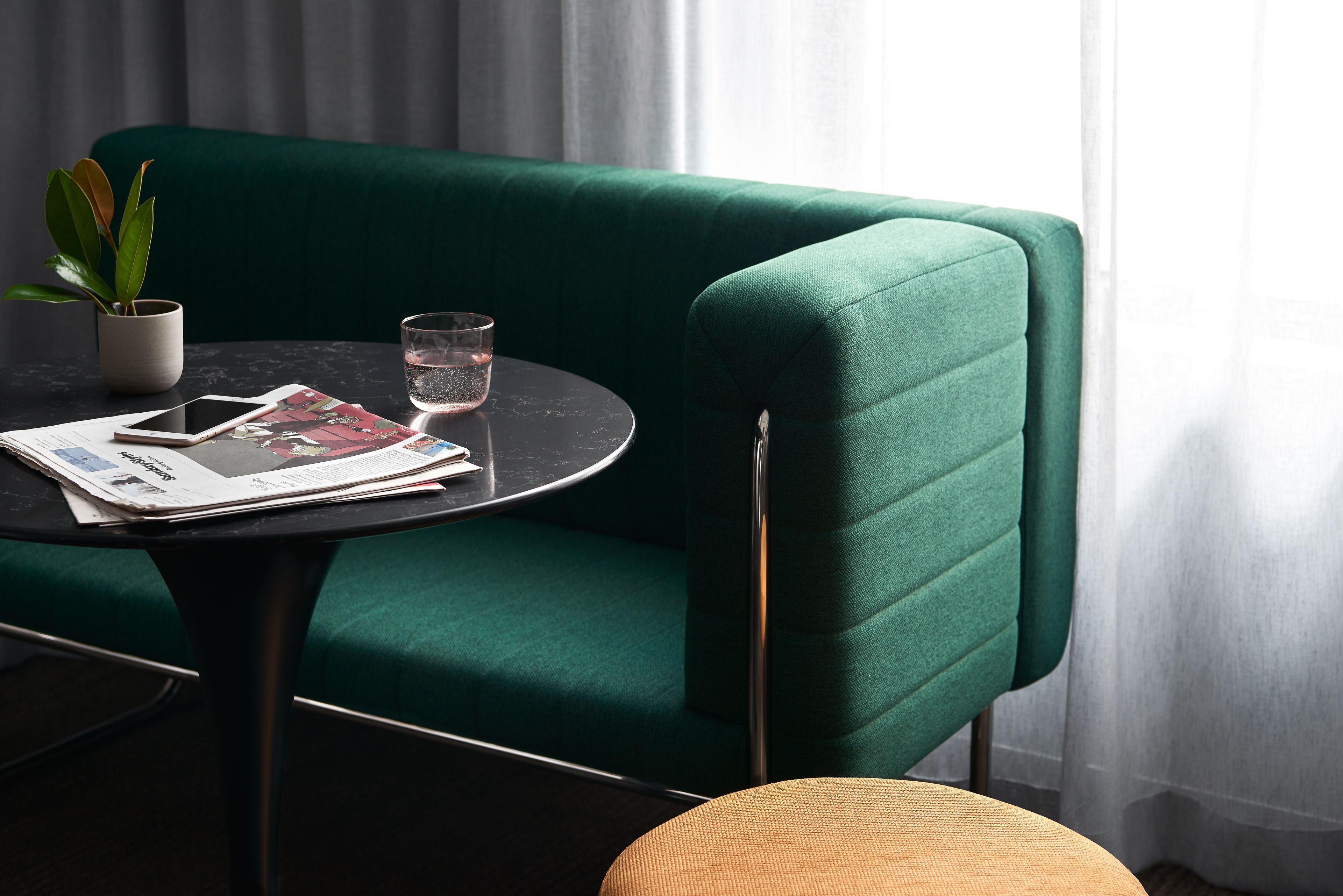 Un canapé vert, une petite table ronde avec un verre d’eau, un téléphone intelligent et un magazine.
