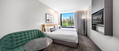 A modern hotel room with a green sofa, a bed with white linens, a flat-screen TV, and a city view.