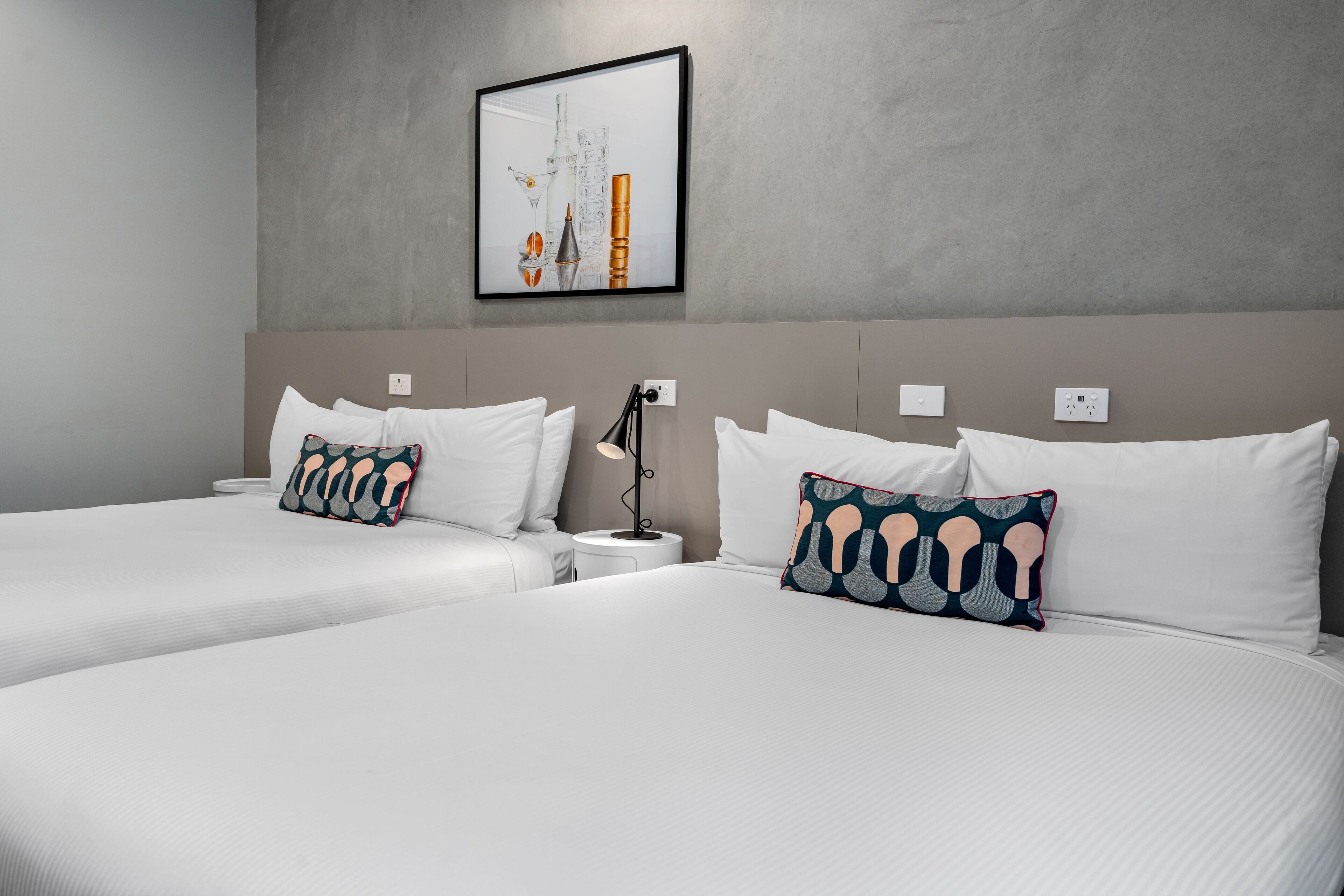 Una habitación de hotel con dos camas, ropa de cama blanca y almohadas estampadas.