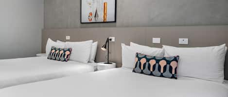 A hotel room with two beds, white bedding, and patterned pillows.