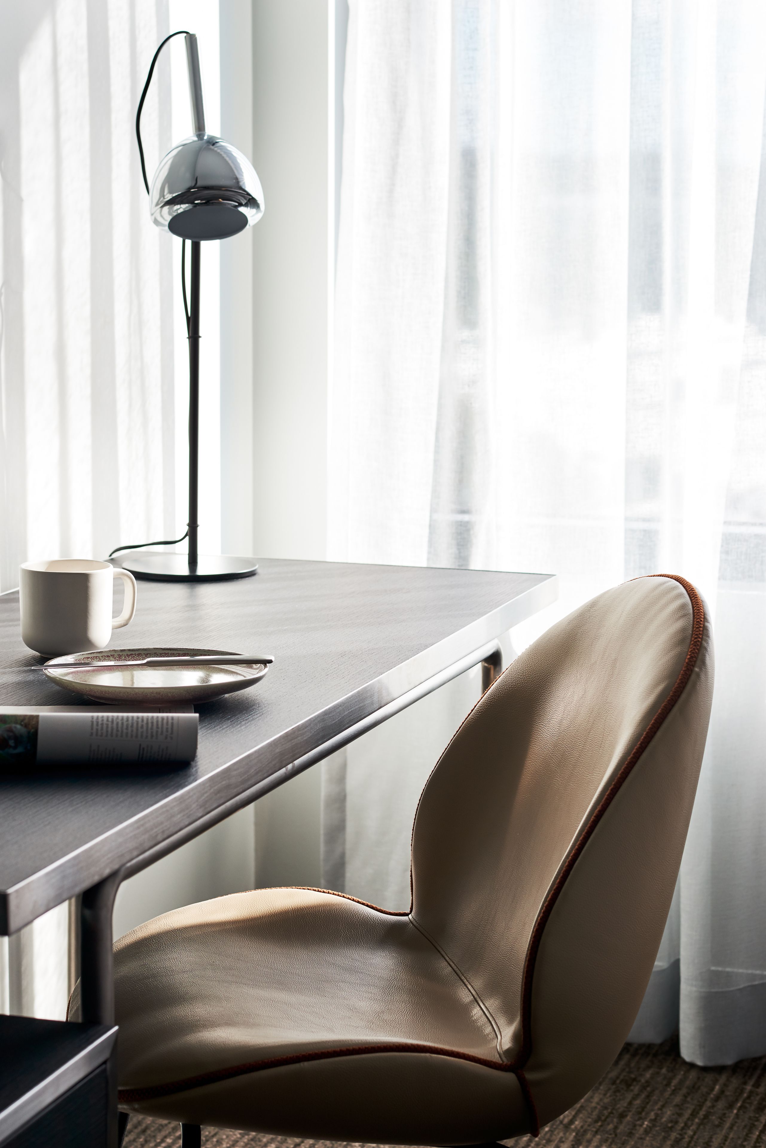 Een moderne kamer met een bureau, een stoel, een lamp en een raam met gordijnen.