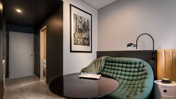 A modern room with a round table, a green tufted chair, a framed cityscape picture, and a bedside lamp.