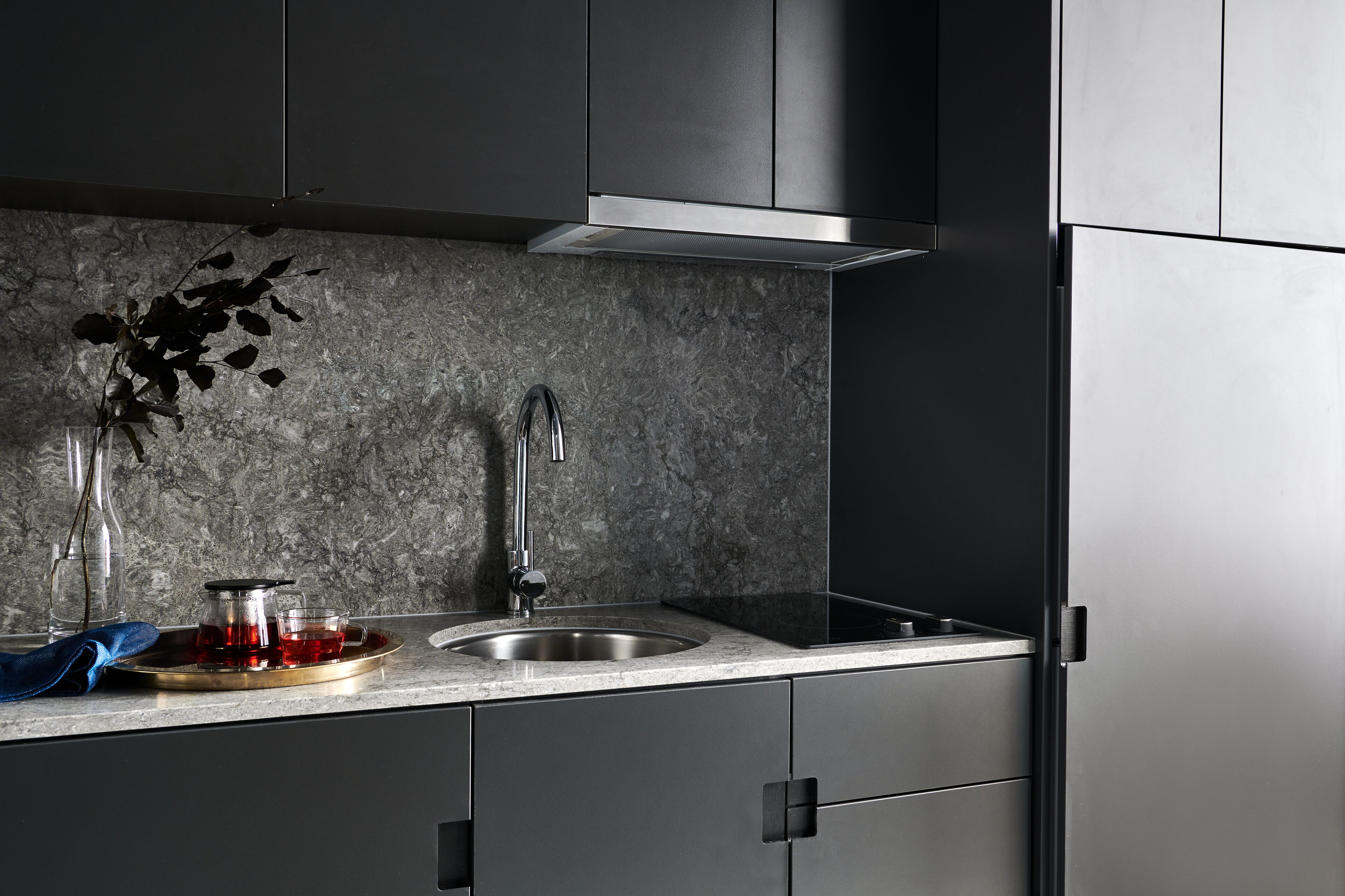 A modern kitchen with dark cabinets, a granite countertop, a stainless steel sink, and a built-in stove.