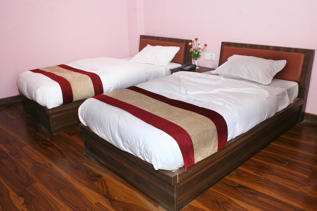 A hotel room with two single beds, wooden headboards, and a wooden floor.