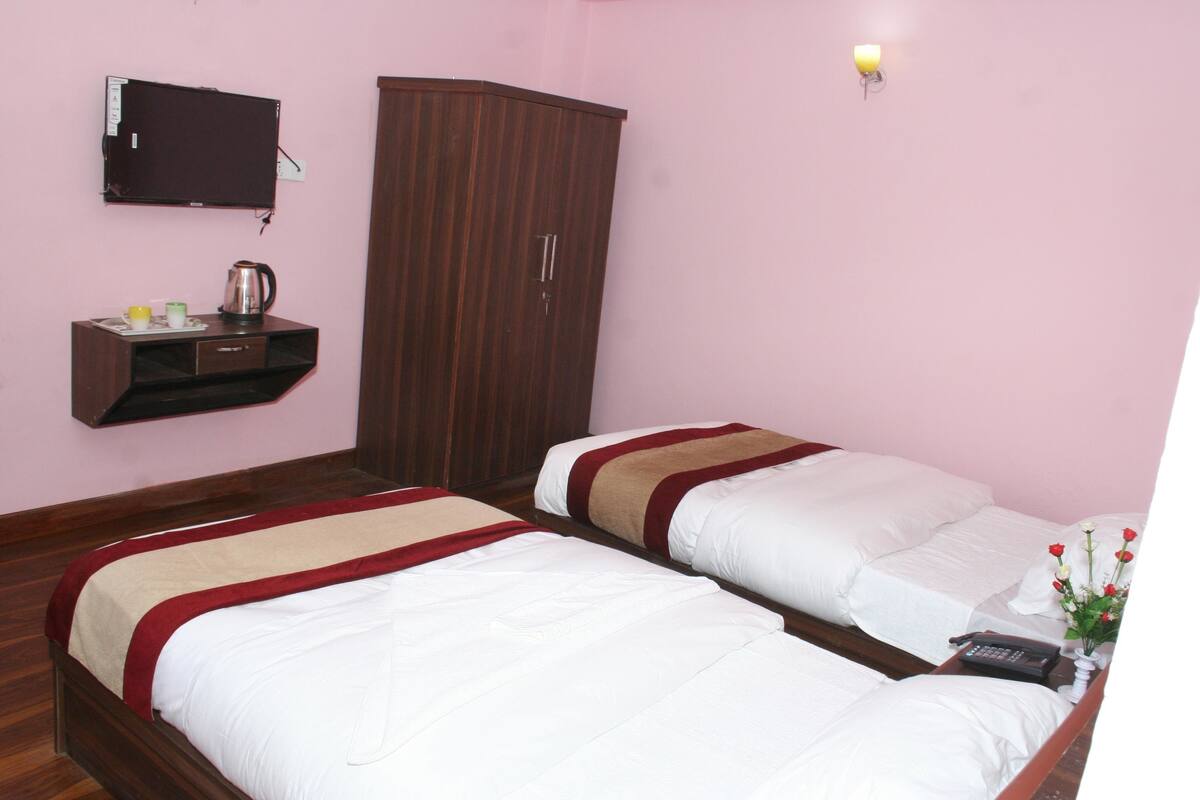 A room with two beds, a wardrobe, a small table with a kettle, and a wall-mounted TV.