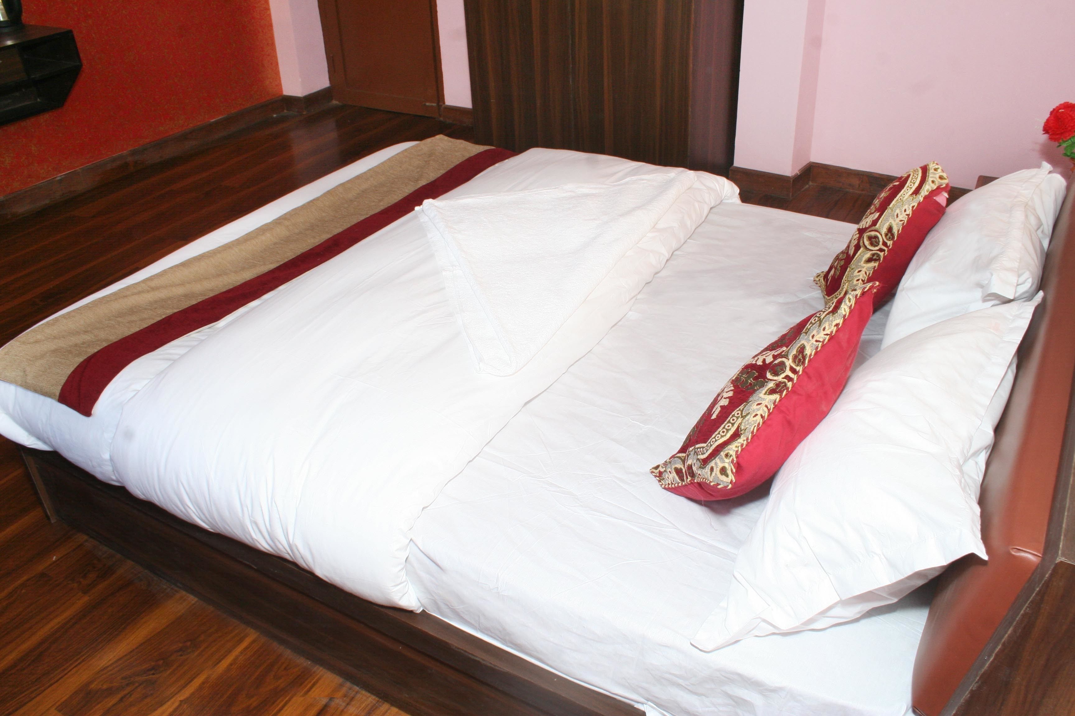 Una cama bien tendida con ropa de cama blanca y roja, un cabecero de madera y suelo de madera.