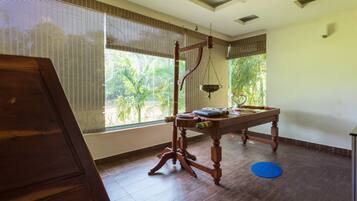Una habitación con una mesa de madera, un ventilador de techo y ventanas grandes con persianas.