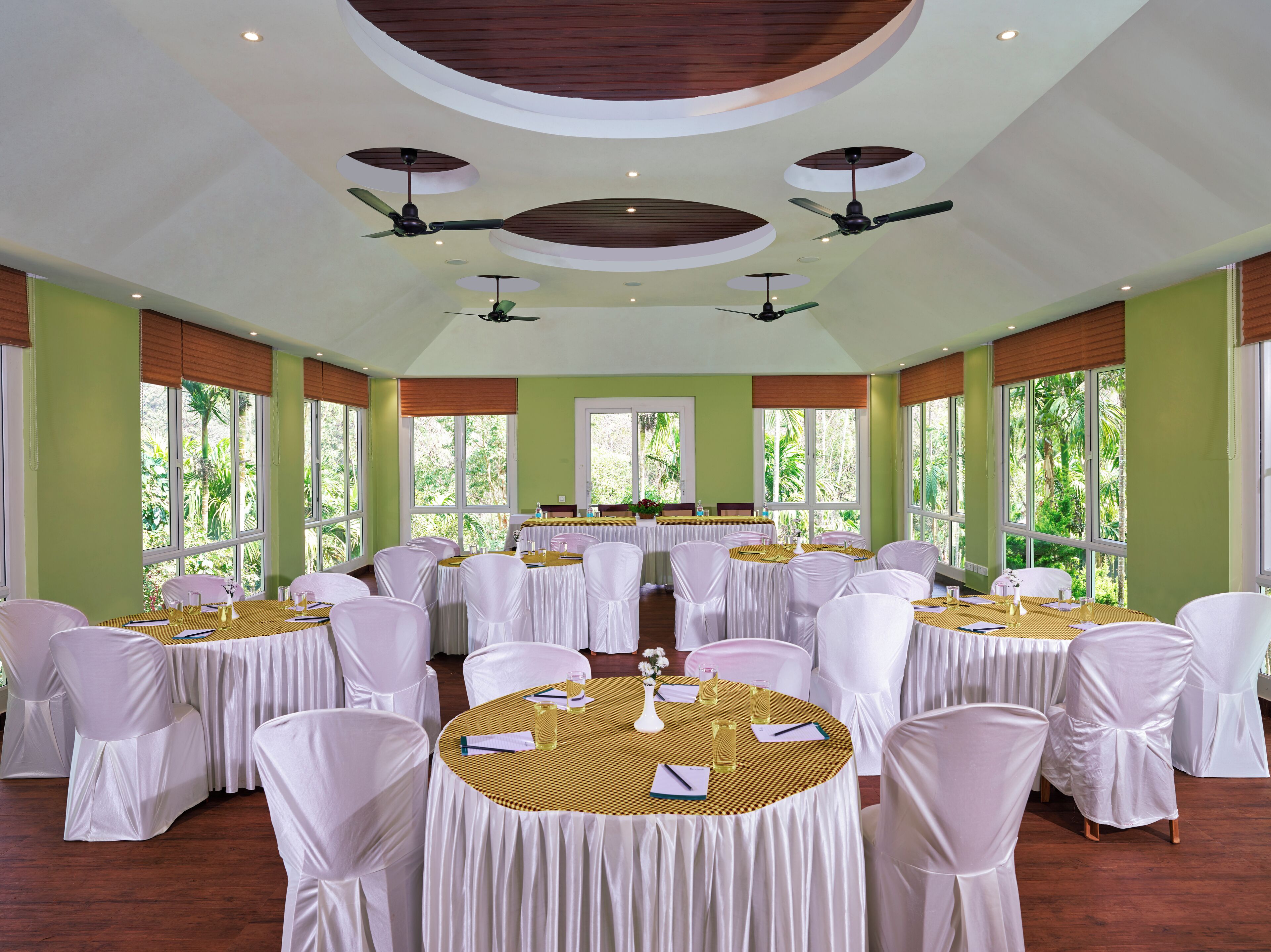 A conference room with round tables, white chairs, and ceiling fans.