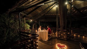 An outdoor dining area with a table set for two, surrounded by wooden railings and benches, under a covered roof structure. - The Woods Resorts Wayanad (Sulthan Bathery)