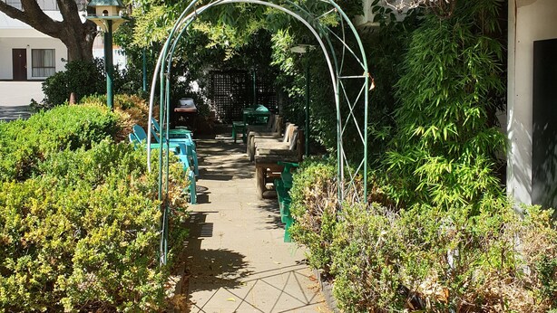 A pathway lined with green plants and benches, leading to a white building. - Arden Motel (North Melbourne)