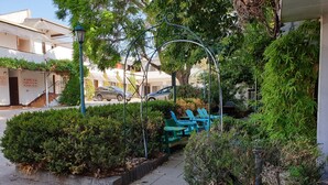 A courtyard with green chairs, a metal archway, and a building with room signs. - Arden Motel (North Melbourne)