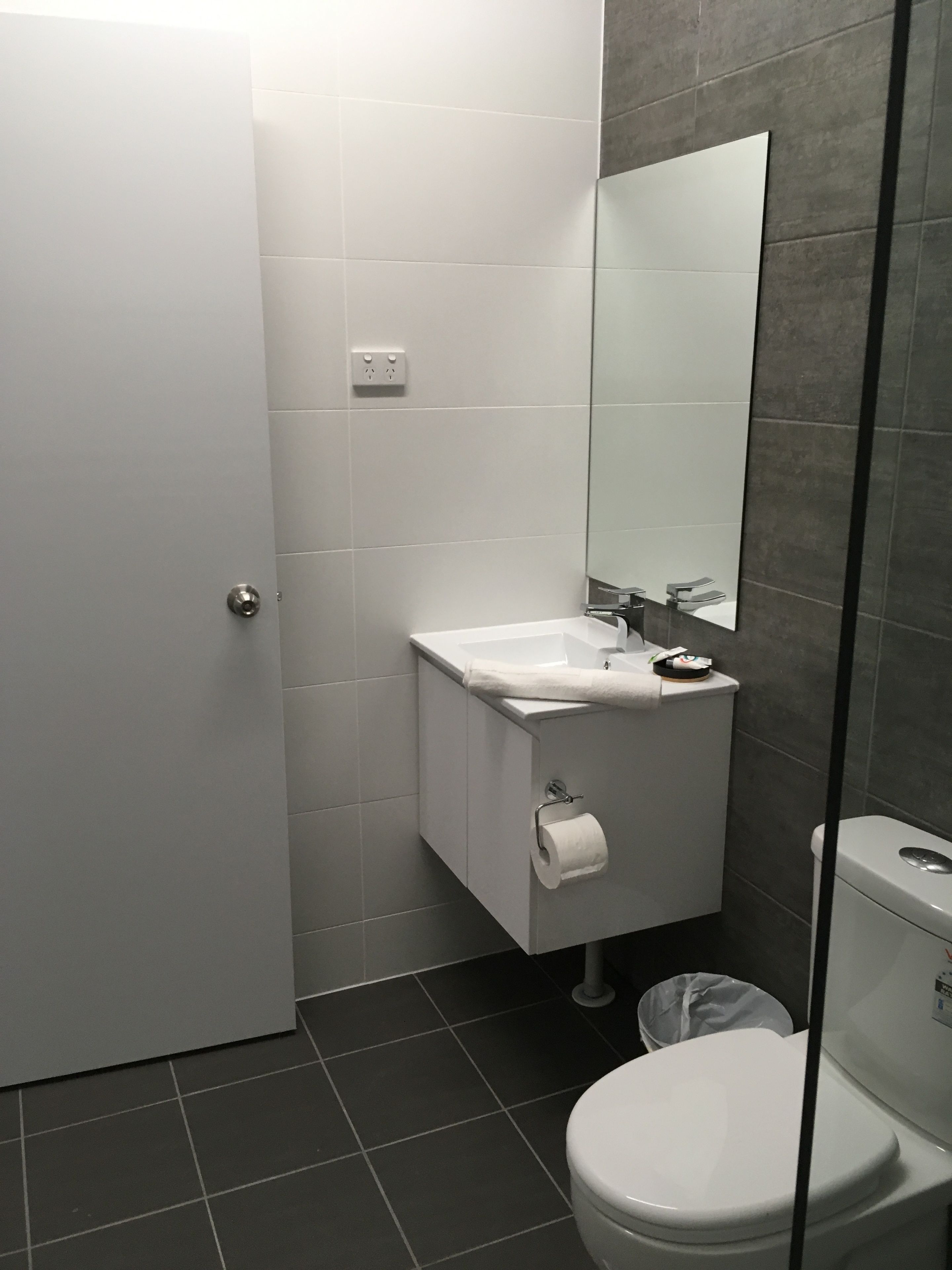 A modern bathroom with a white toilet, a sink with a mirror above it, and a trash bin.