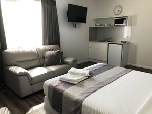 A hotel room with a sofa, a bed, a flat-screen TV, a microwave, and a small kitchenette. - Escape On Lake (Cairns)
