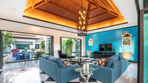 Ein modernes Wohnzimmer mit Schachbrettmuster-Boden, zwei blauen Sofas, einem Glastisch und einer Holzbalkendecke.