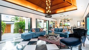 Ein geräumiges Wohnzimmer mit Schachbrettmuster-Boden, einem großen Ecksofa, einem schwarzen Samt-Sessel und einem Glastisch.