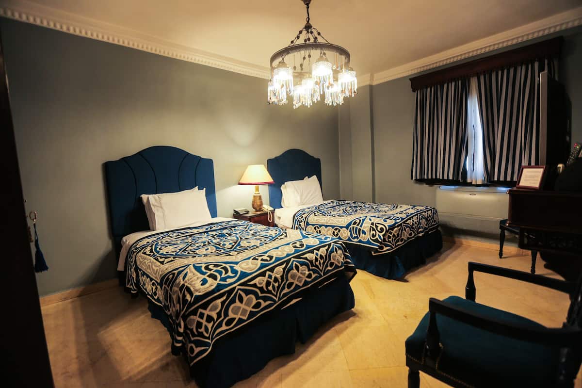 Hotellihuone, jossa on kaksi sänkyä, kattokruunu, työpöytä ja näkymä ulos.