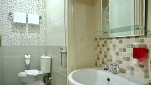 A modern bathroom with a glass shower enclosure, a white sink, and a toilet. - Style50 homestay (Surabaya)