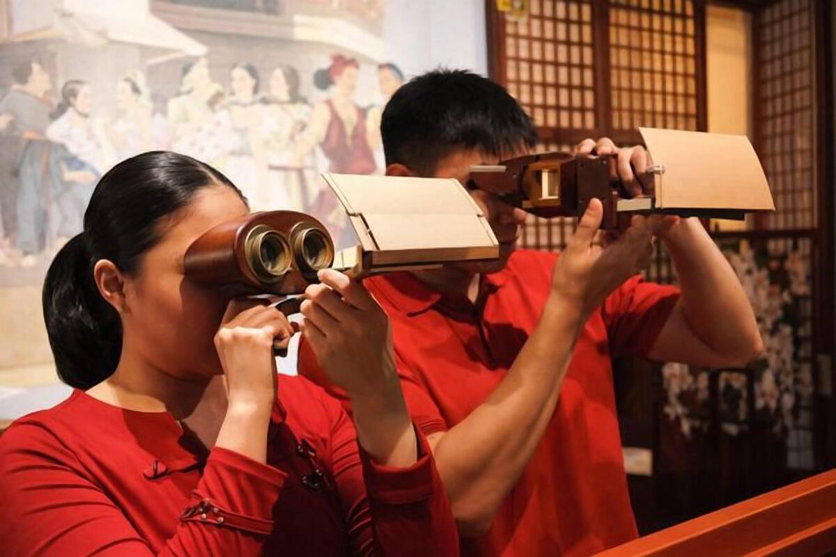 Two individuals in red shirts using binoculars to look at a display.