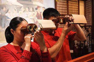 Dos personas con camisetas rojas usando binoculares para observar una exhibición.