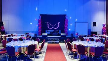 A conference room with round tables, red chairs, and a stage with a neon wing design.