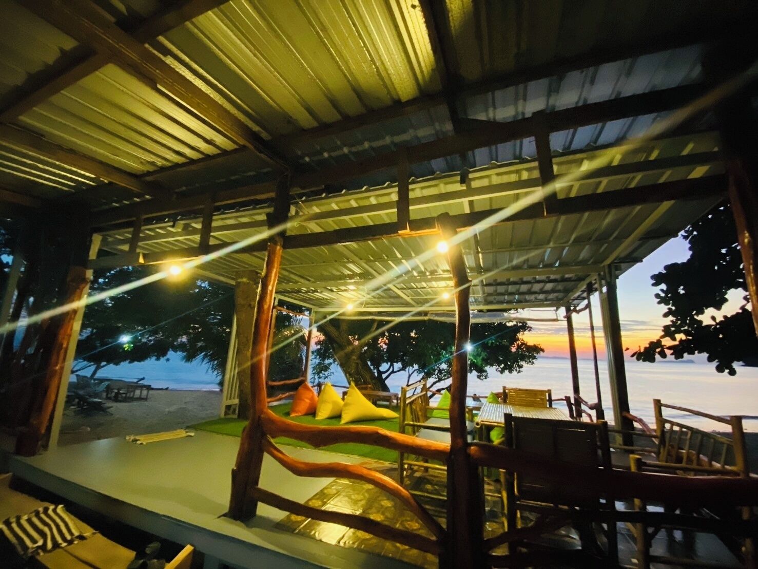 Un espace extérieur aménagé avec un toit abrité, du mobilier en bois et une vue sur le coucher du soleil.