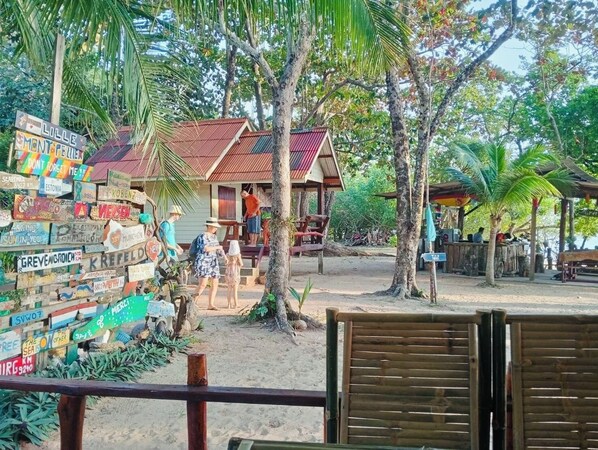 A rustic wooden house with a red roof, surrounded by palm trees and a collection of colorful signs. - Koh Phu Valley (Nuea Khlong)