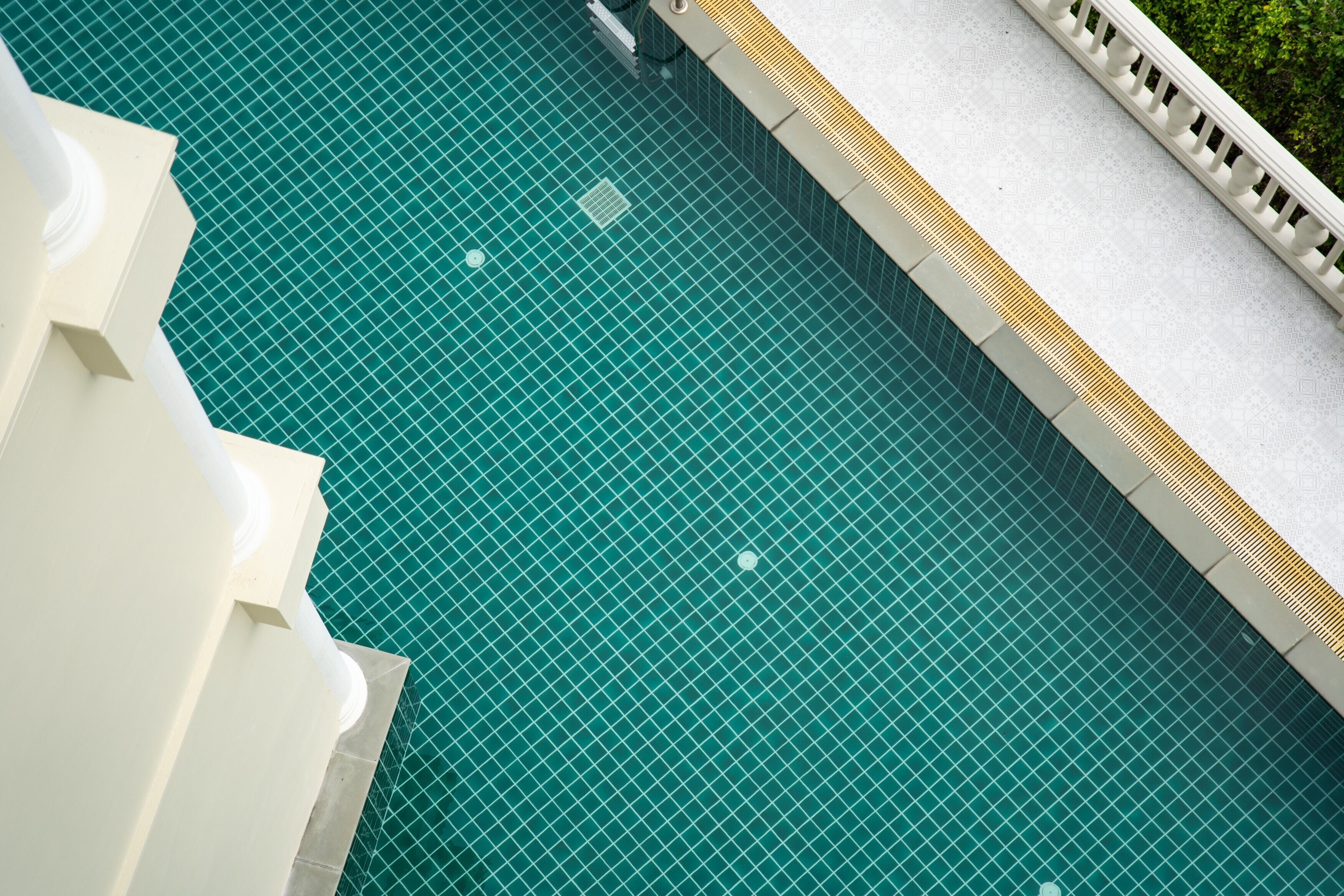 A view of a swimming pool with a tiled floor and a white structure with steps leading down to the pool.