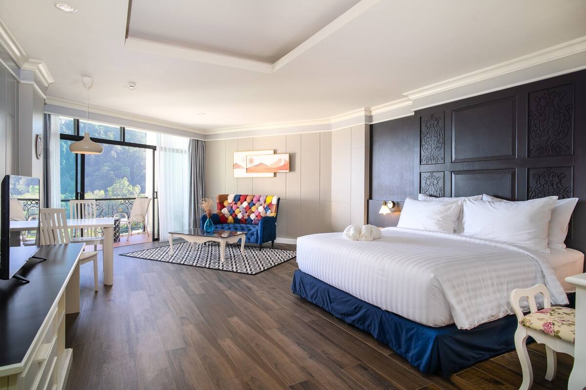 Habitación de hotel con una cama grande, un escritorio y un balcón con sillas.