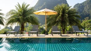 A poolside area with lounge chairs and a palm tree, surrounded by lush greenery and mountains. - Heaven View Krabi (Krabi)