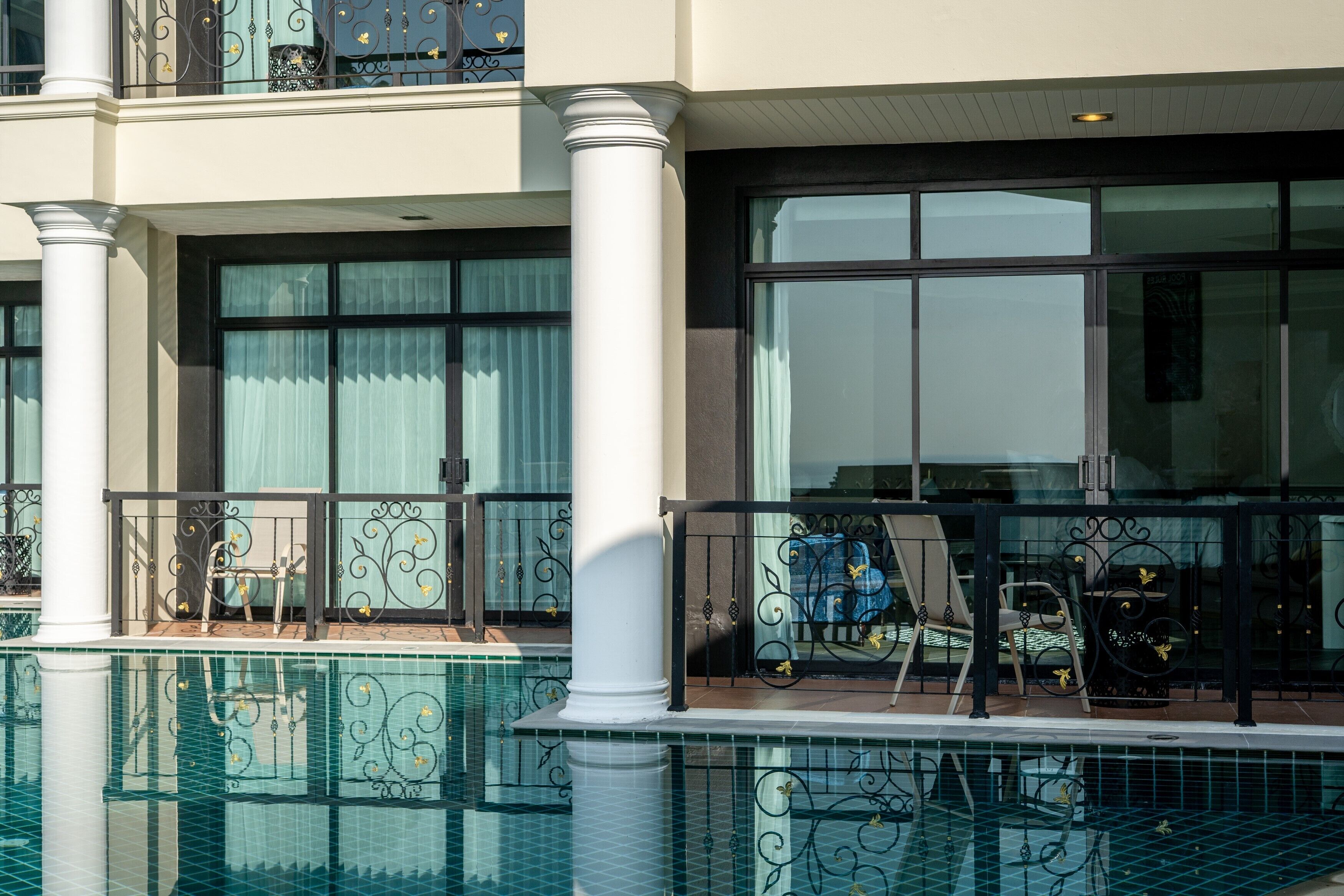 A poolside area with a glass balustrade, a lounge chair, and a table with a chair.