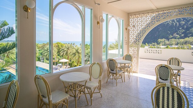 A terrace with wicker chairs and tables, large arched windows, and a view of a pool and greenery. - Heaven View Krabi (Krabi)