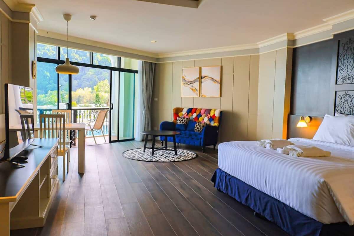Una habitación de hotel con una cama grande, un escritorio con una silla, un sofá y un balcón con vistas a árboles.