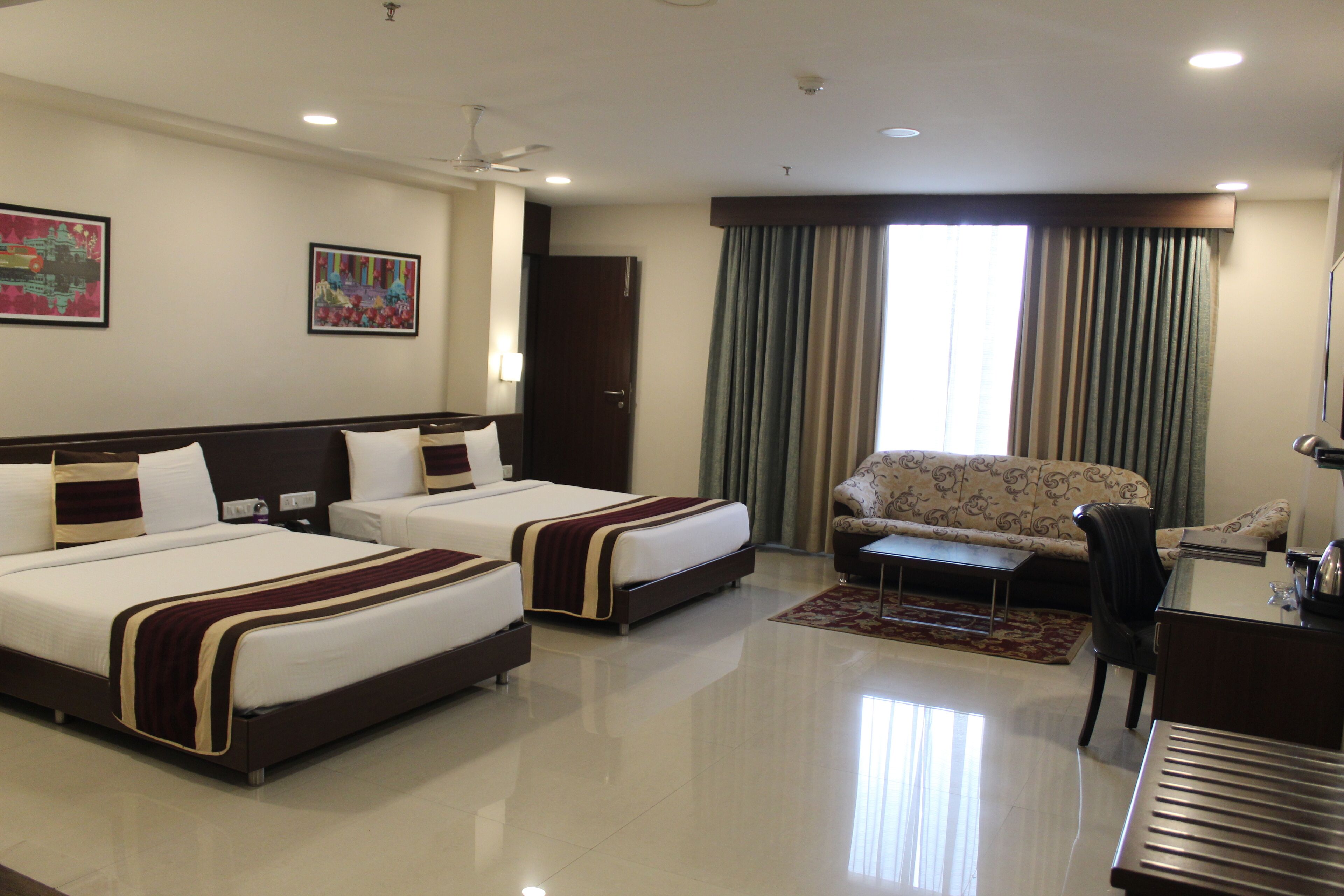 A hotel room with two beds, a sofa, a desk, and a chair.