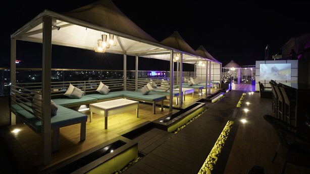 A rooftop lounge area with multiple seating arrangements under a canopy, a pathway, and a view of the cityscape. - Brilliant Hotel & Convention Center (Indore)