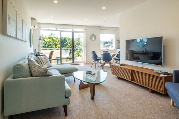 Relax in this stylish living room with a sofa, coffee table, and TV, leading to an outdoor space with city views.