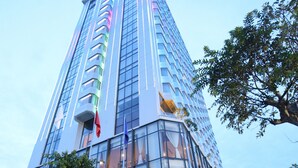 A modern high-rise building with a glass facade, surrounded by trees and a well-maintained garden. - Central Luxury Ha Long Hotel (Bai Chay)