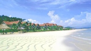 A beach with thatched-roof buildings and a sandy shoreline. - Central Luxury Ha Long Hotel (Bai Chay)
