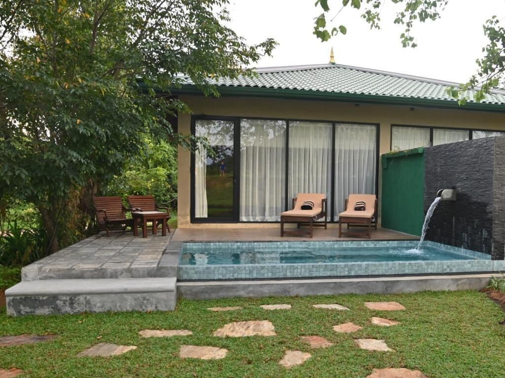 A house with a swimming pool, two lounge chairs, and a stone wall.