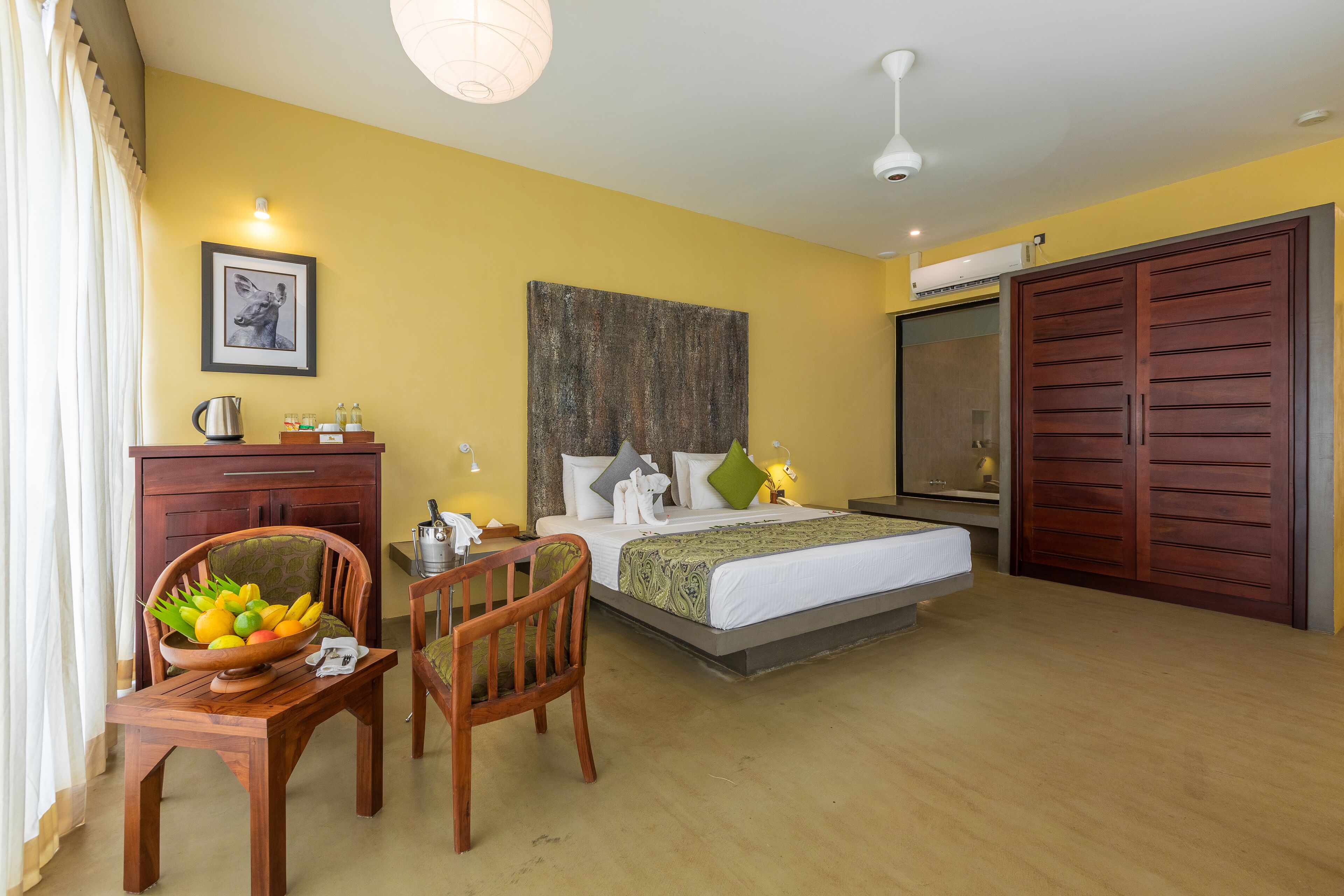 Habitación de hotel con cama, una silla de madera, una mesa con frutero, un cuadro en la pared y un armario.
