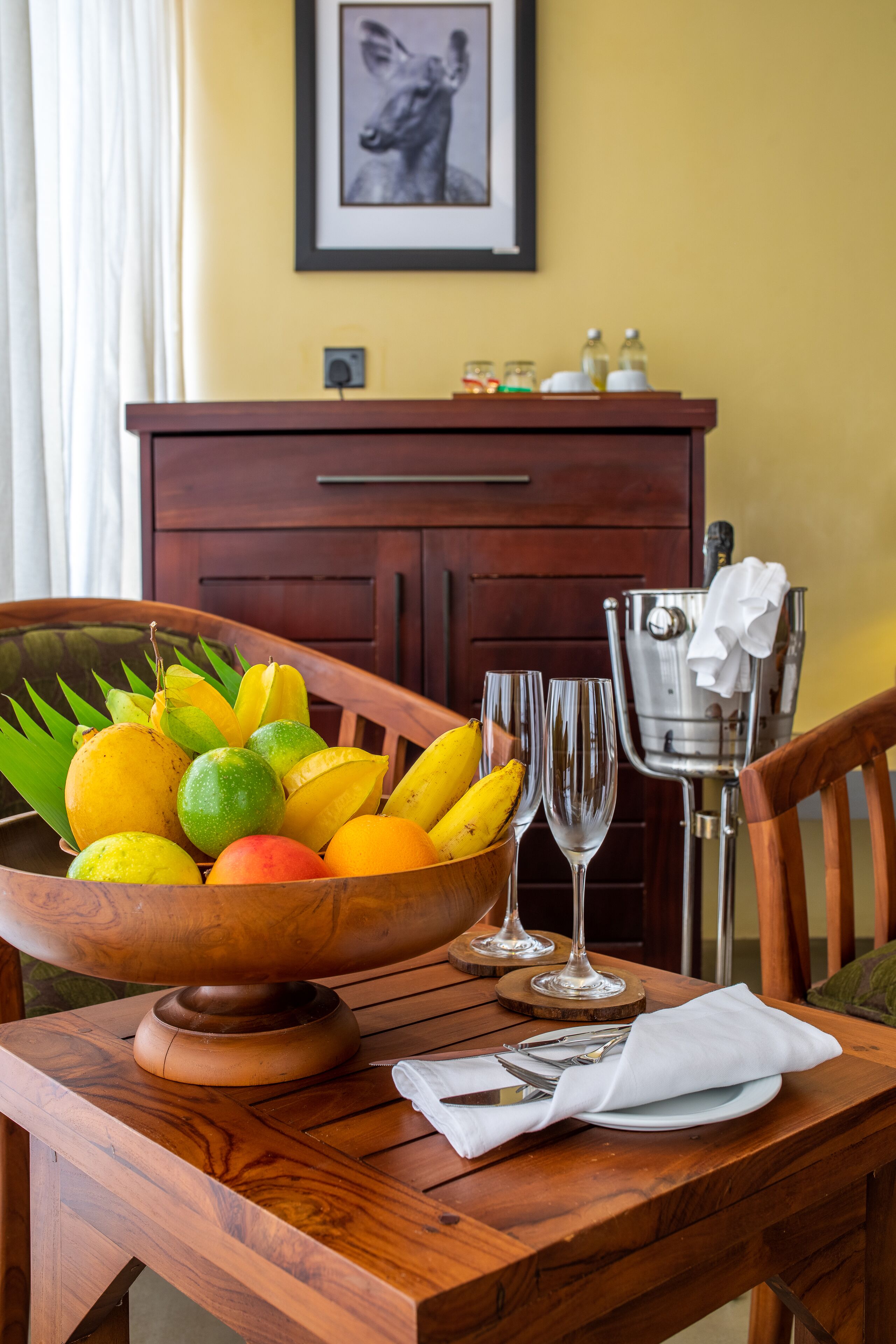 A wooden dining table with a fruit bowl, two wine glasses, and a napkin.