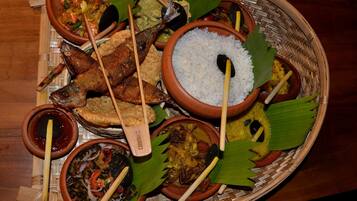 Una variedad de platos servidos en una cesta tejida, incluyendo arroz, pescado y otras preparaciones diversas, junto con utensilios de madera.