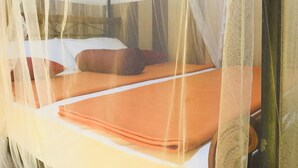 A bed with a mosquito net and a folded orange blanket. - Ella City Reach Hostel (Ella)