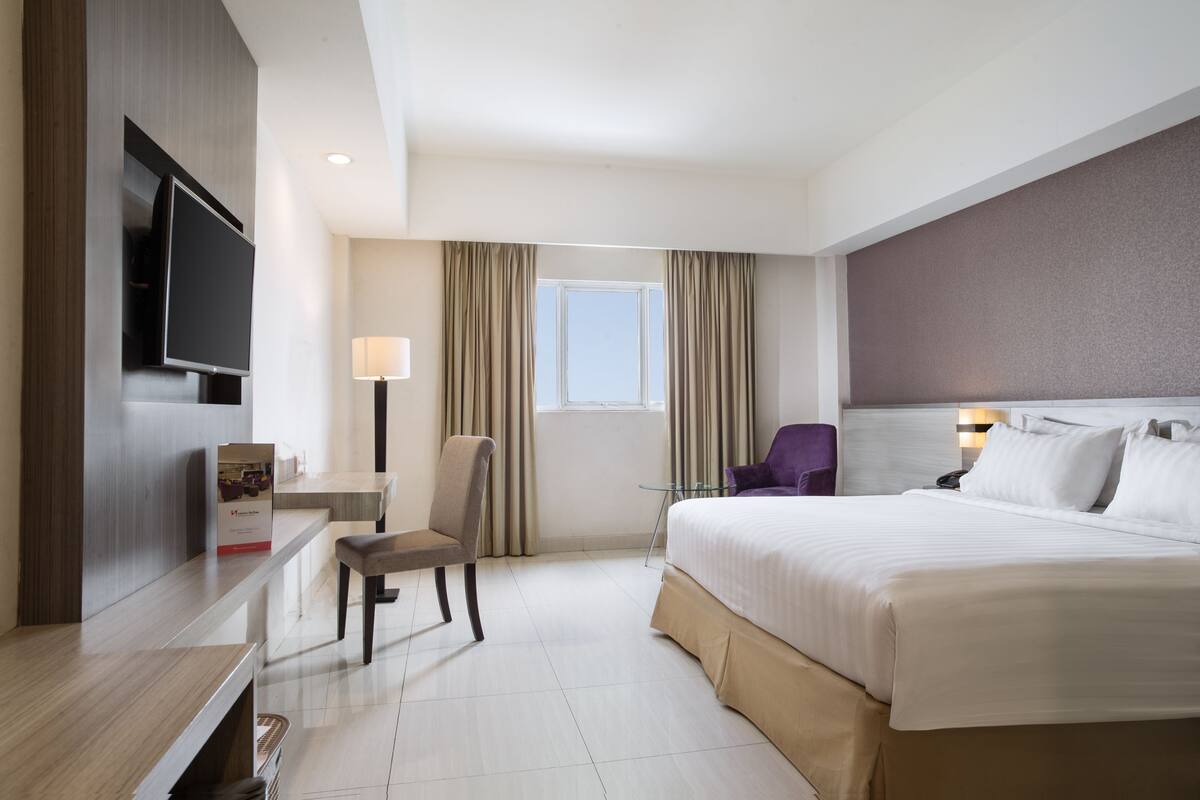 Une chambre d’hôtel équipée d’un lit, d’un bureau, d’une chaise, d’une télévision, d’une lampe et d’une fenêtre avec des rideaux.