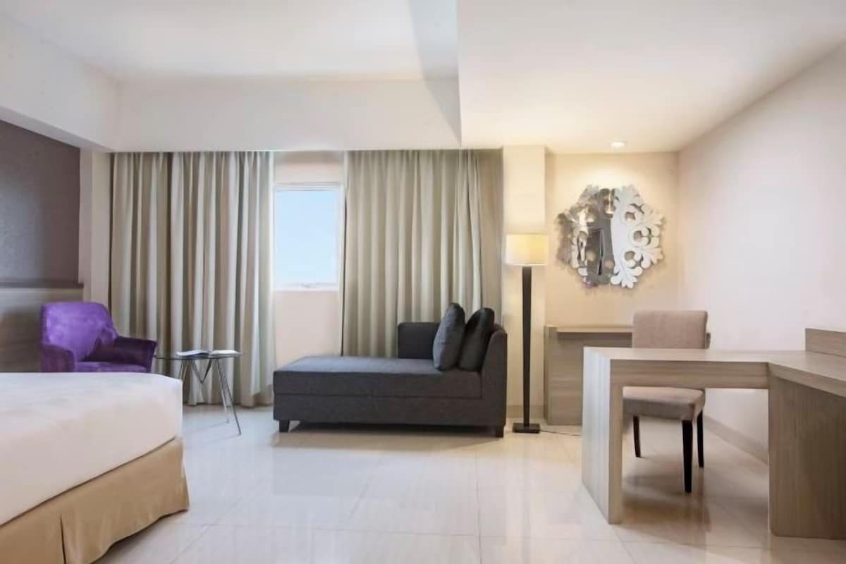 Una habitación de hotel con cama, sofá, escritorio, silla, lámpara y un adorno de pared.