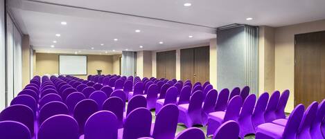 A conference room with rows of purple chairs and a projection screen at the front.